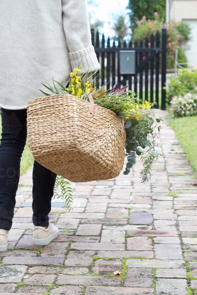 Woman with market basket of wild flowers walking along footpath - Australian Stock Image