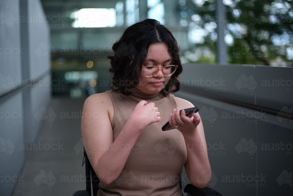 Woman with short hair wearing glasses and brown tank top looking at her mobile phone - Australian Stock Image