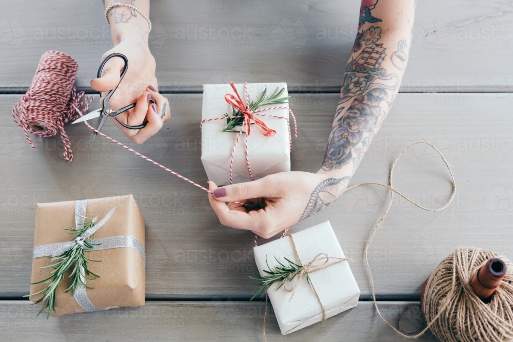 Woman with sleeve tattoo cutting twine while wrapping gifts - Australian Stock Image
