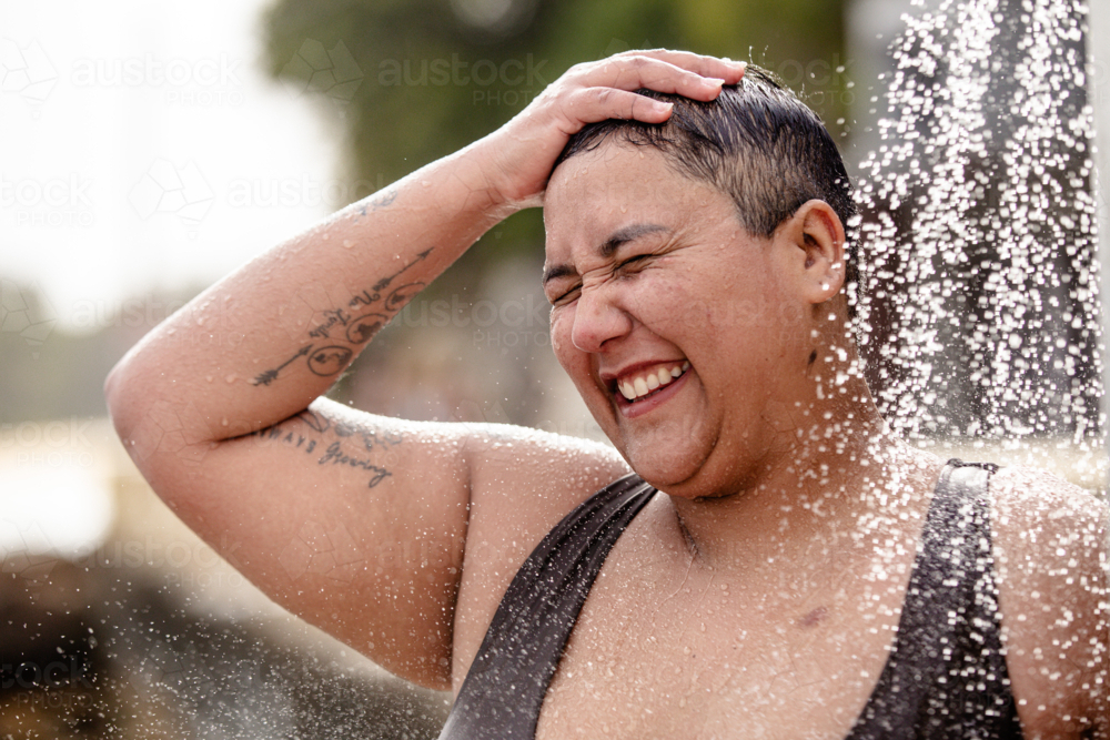 Woman with tattoos standing under an outdoor shower - Australian Stock Image