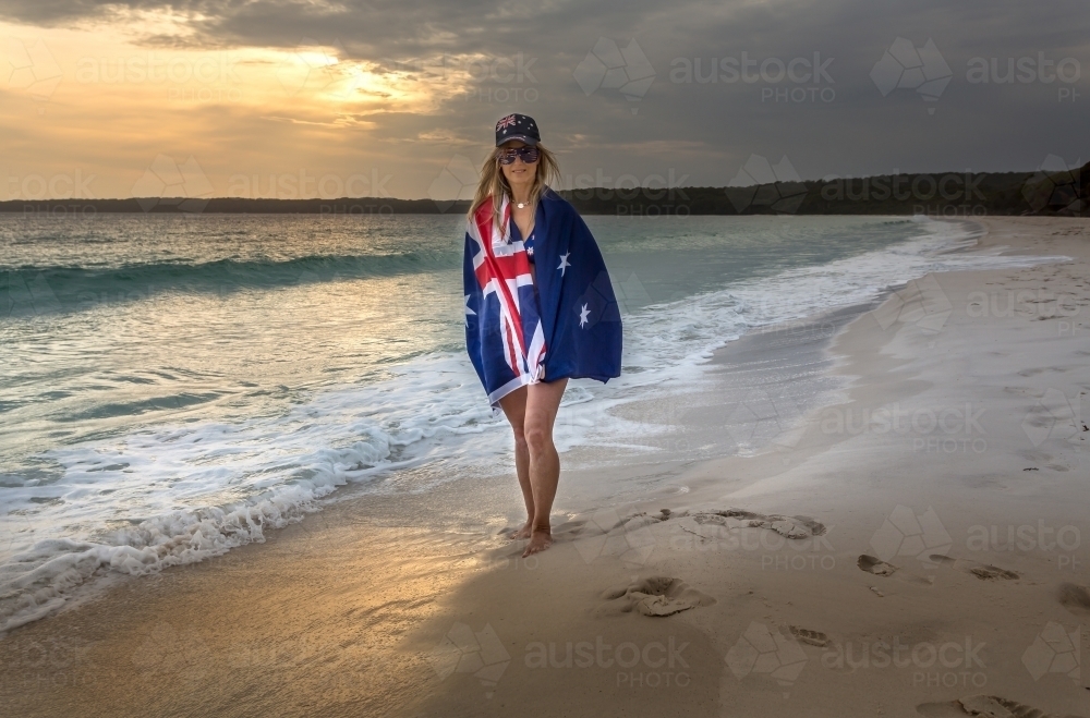 Woman with the Australian flag wrapped around, wears a hat and sunglasses - Australian Stock Image