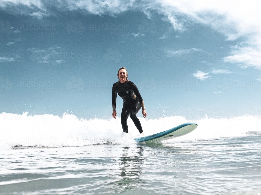 Women catching whitewash wave on longboard soft board looking at camera smiling - Australian Stock Image