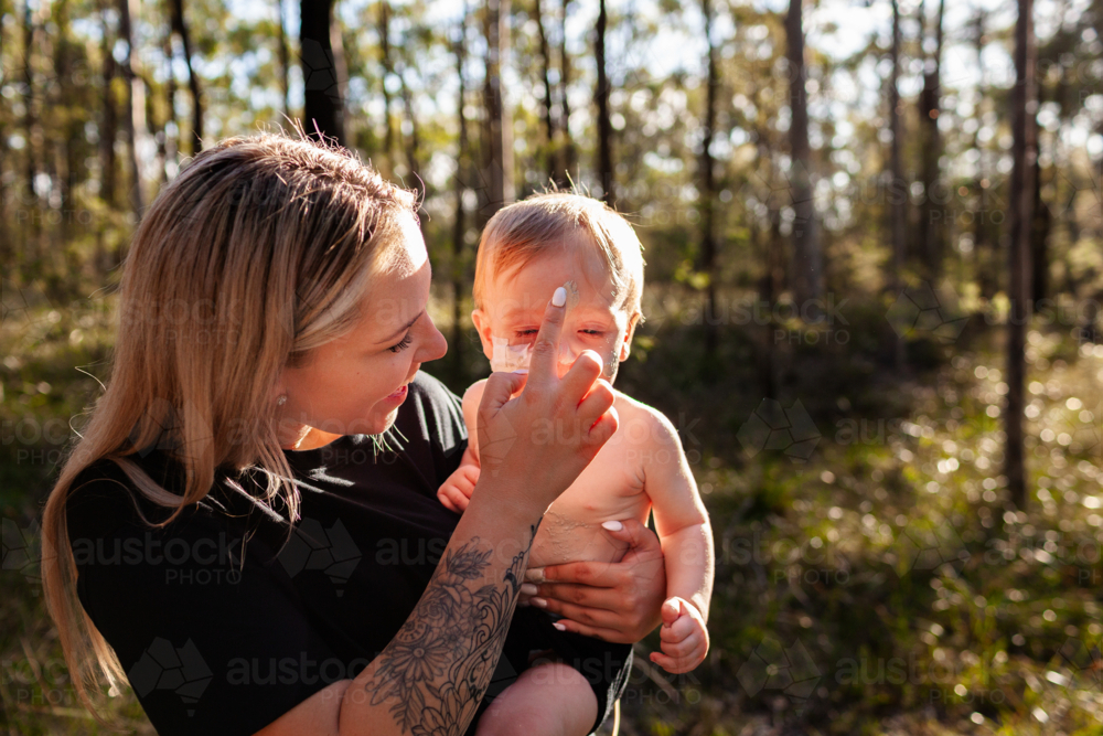 Wonnarua Aboriginal woman holding baby boy painting his face with ochre body paint - Australian Stock Image