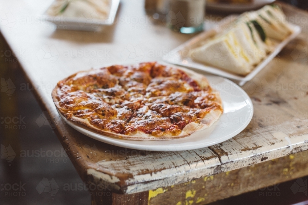 Wood fired pizza and wooden table, sandwiches in background - Australian Stock Image