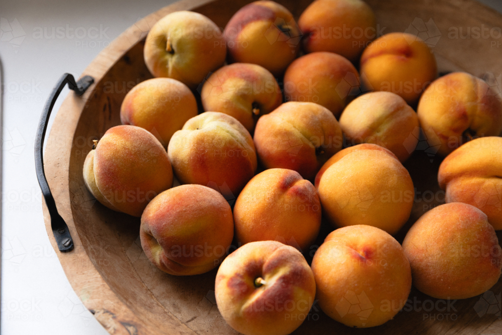 Wooden bowl full of freshly picked ripe peaches on kitchen bench in natural window light - Australian Stock Image