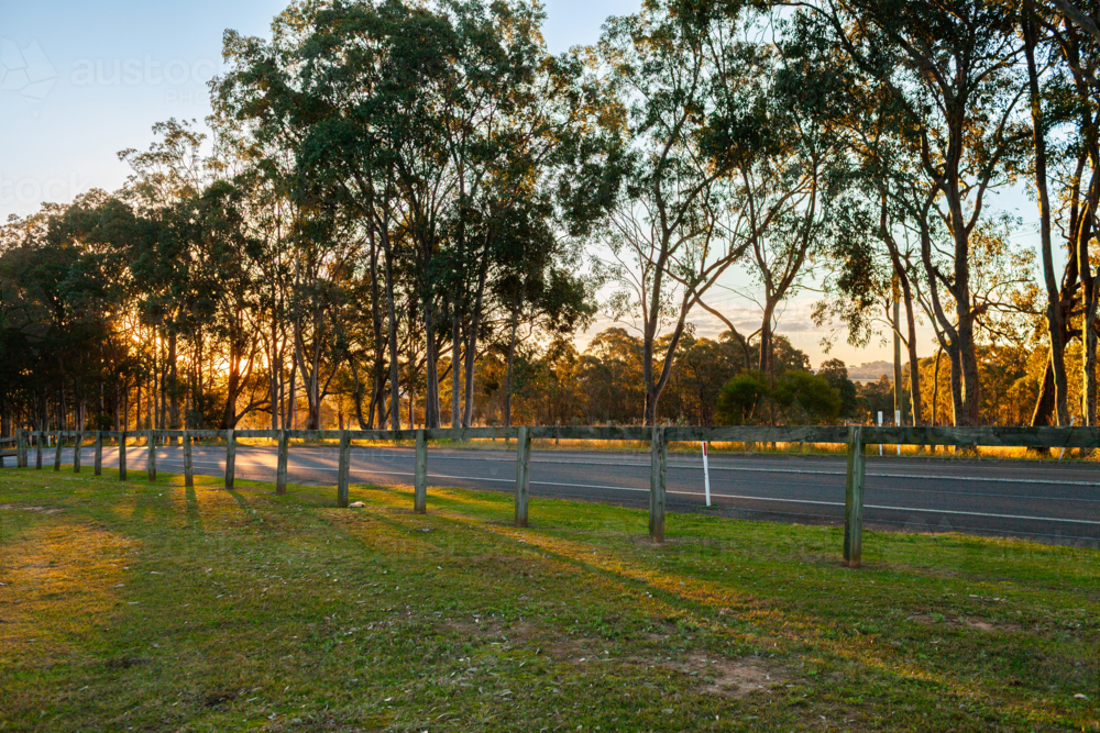 wooden fence along roadside at sunset with long shadows from gum trees - Australian Stock Image