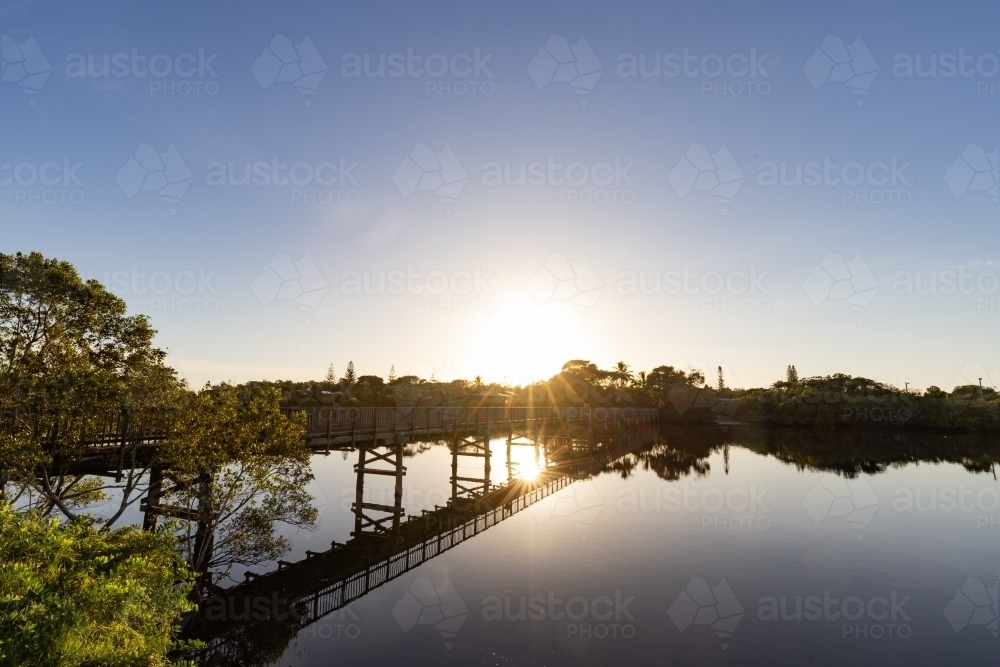 Wooden footbridge leading across Simpsons Creek at Brunswick Heads at sunrise - Australian Stock Image