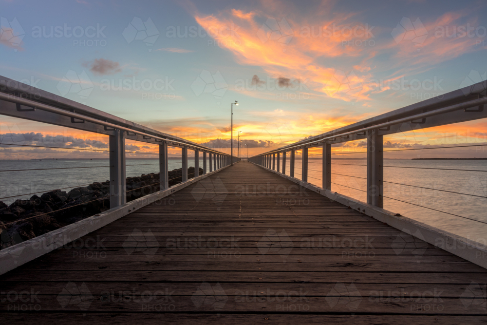 Wooden jetty stretching over water with cloudy sunrise sky - Australian Stock Image