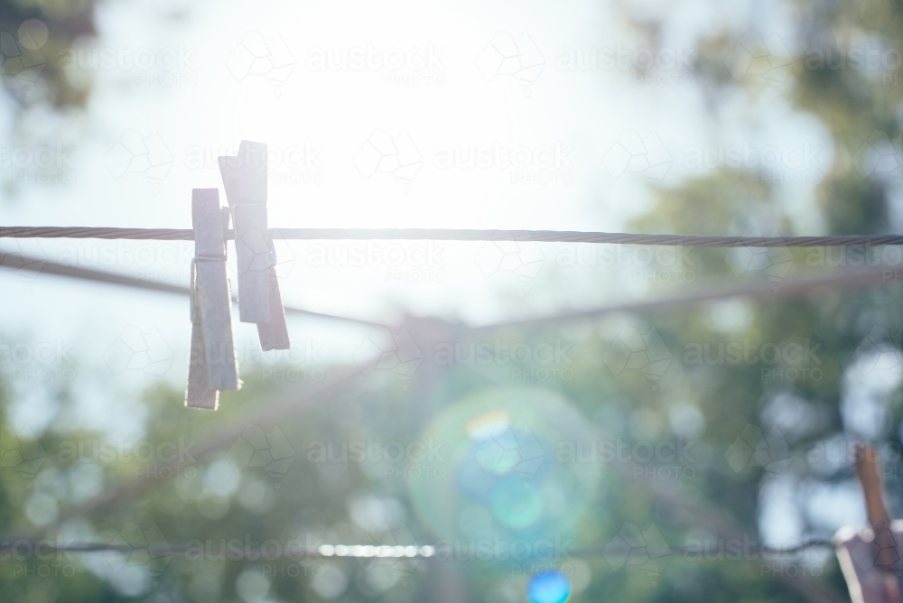 Wooden pegs on clothesline with sun flare - Australian Stock Image