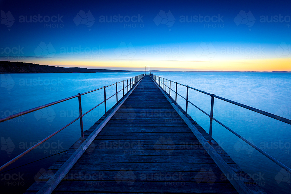 Wooden pier stretching into the calm sea at dawn - Australian Stock Image