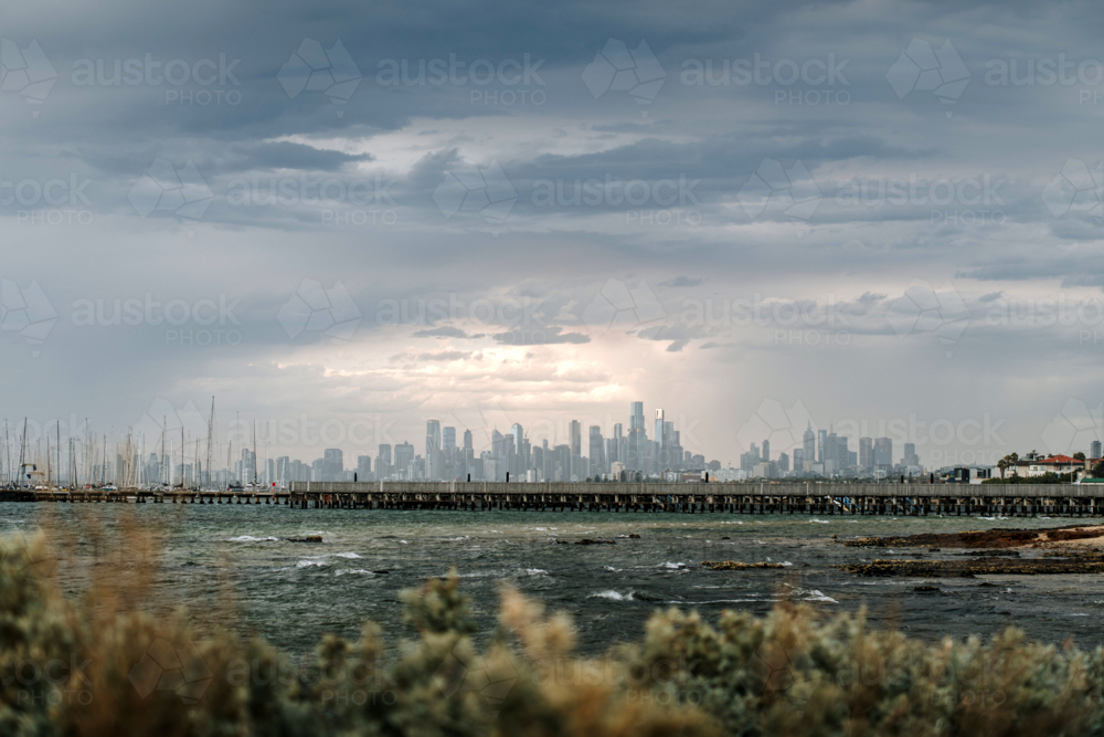 Wooden pier stretching toward city skyline under cloudy sky - Australian Stock Image