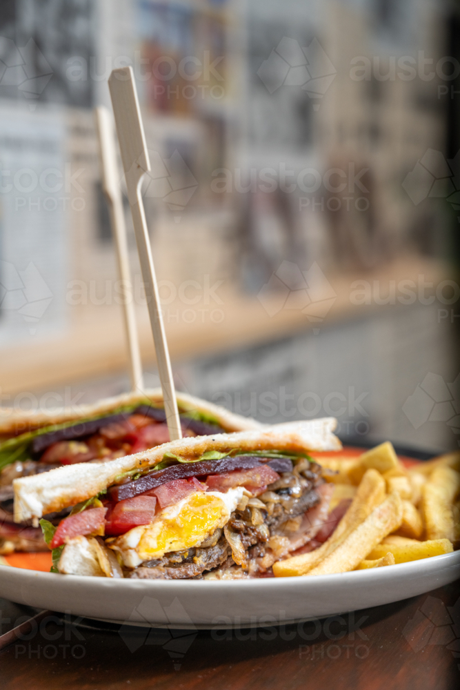 Wooden skewers pierce through the layers of a club sandwich with fries on the side - Australian Stock Image