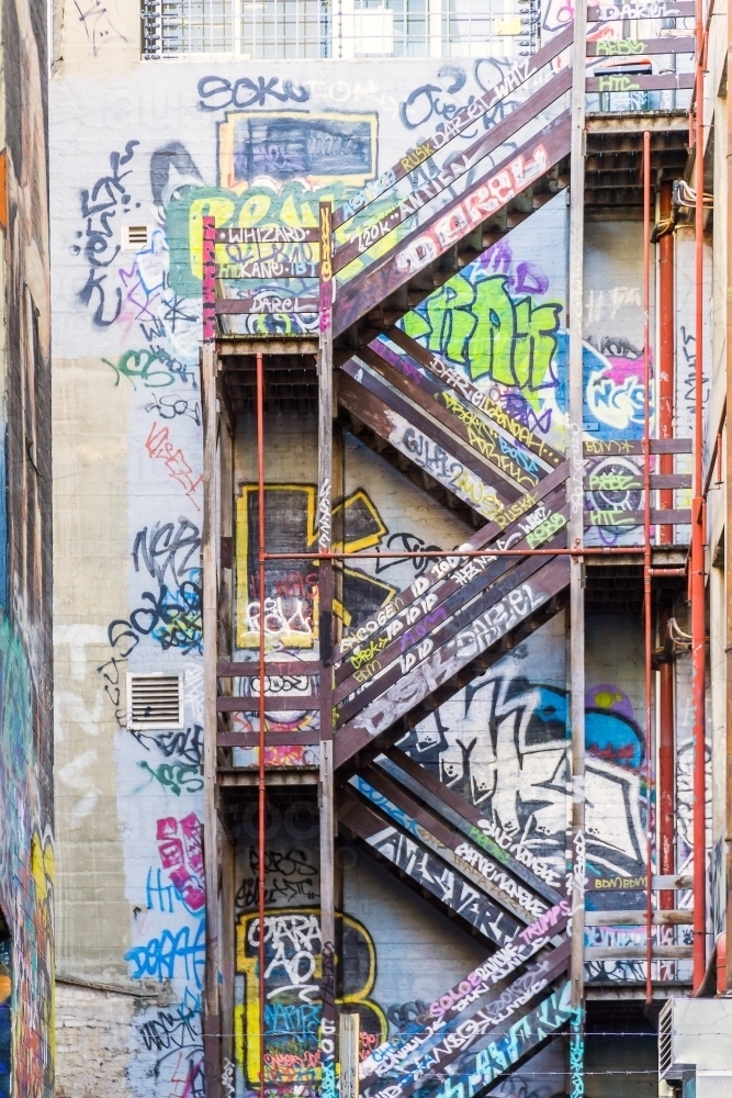 Wooden stairs going up the side of a graffiti covered wall - Australian Stock Image