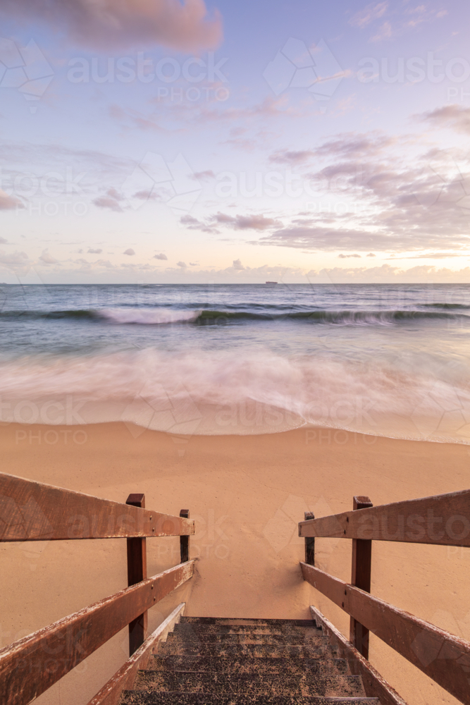 Wooden stairs leading to beach at sunset with waves breaking - Australian Stock Image