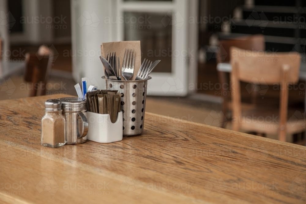 Wooden table waiting for customers with cutlery, serviettes and sugar satchels in the centre - Australian Stock Image