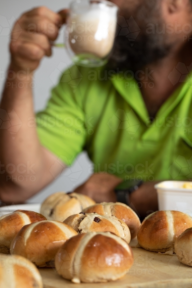 worker drinking coffee with hot cross buns in foreground - Australian Stock Image