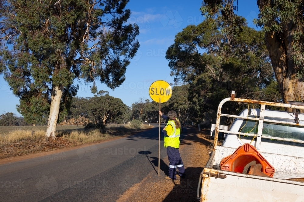 worker holding road work lollipop slow down sign on country road - Australian Stock Image