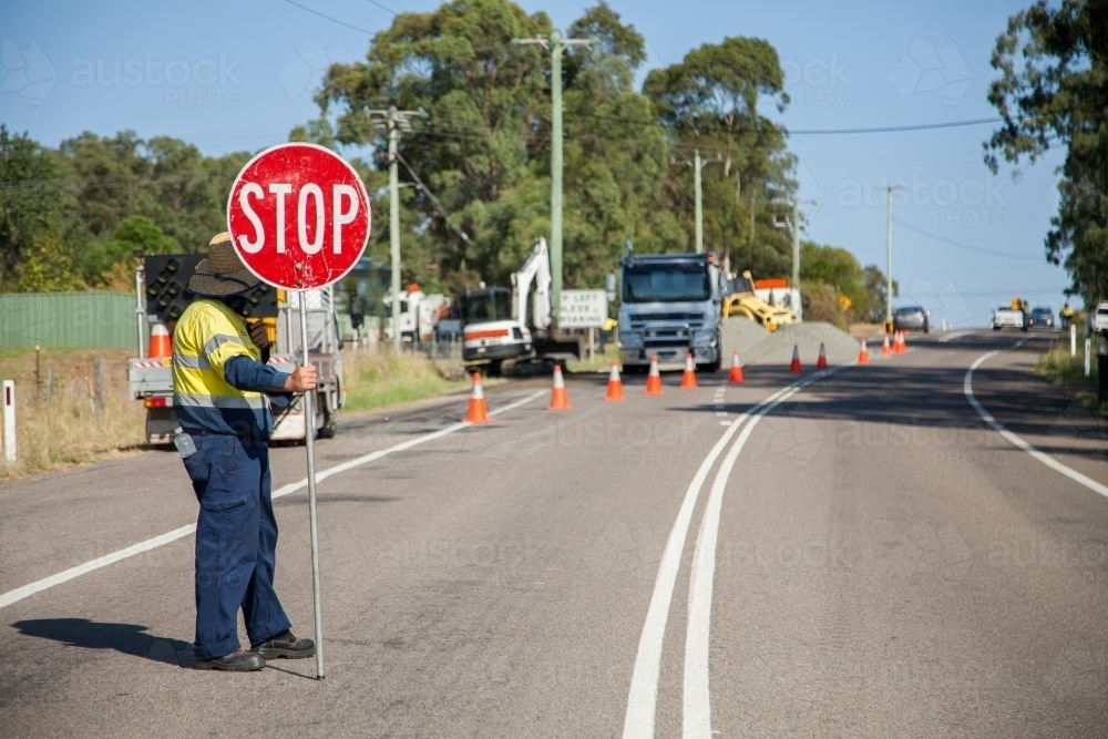 Worker in hi-vis holding roadwork stop sign - Australian Stock Image