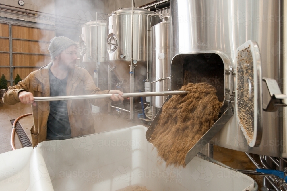 Worker removing waste mash from stainless steel tanks - Australian Stock Image