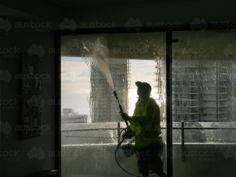 Worker using a pressure hose to clean the windows of an apartment building - Australian Stock Image