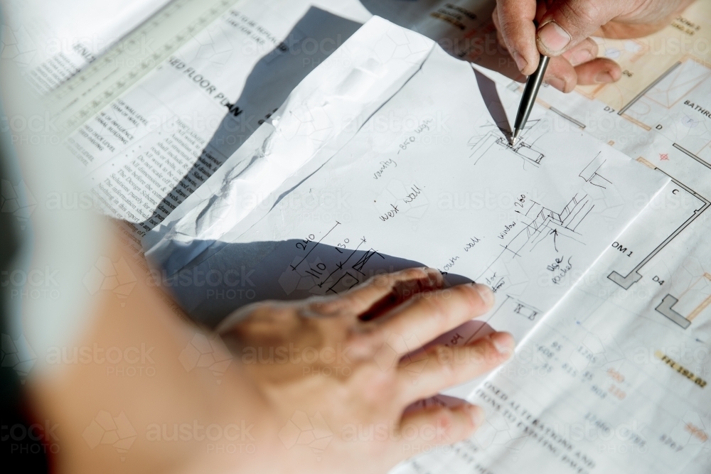 Workers' hands on building plans at a construction site - Australian Stock Image