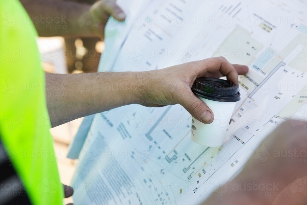 Workers' hands on building plans at a construction site - Australian Stock Image