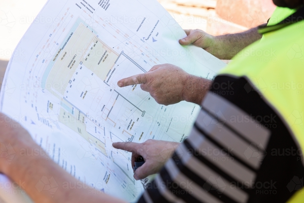 Workers' hands pointing to building plans at a construction site - Australian Stock Image