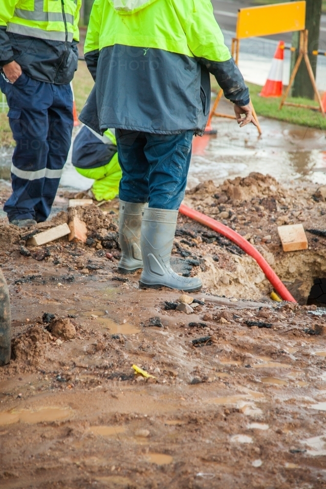 Workers in hi-vis clothing standing around a muddy hole - Australian Stock Image