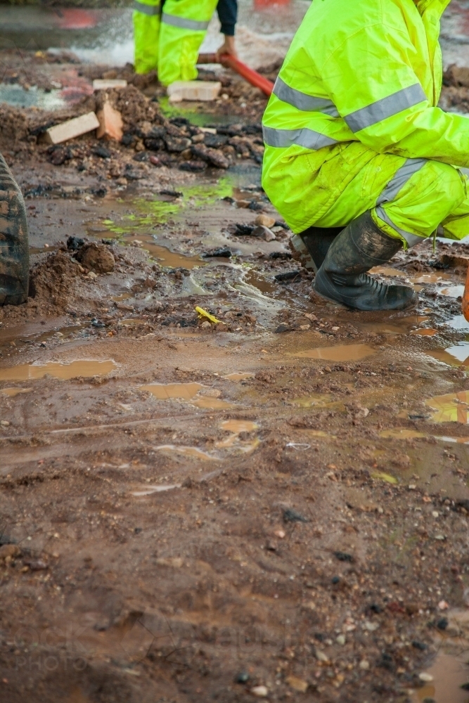 Workers in hi-vis gear around a mud hole in the road - Australian Stock Image