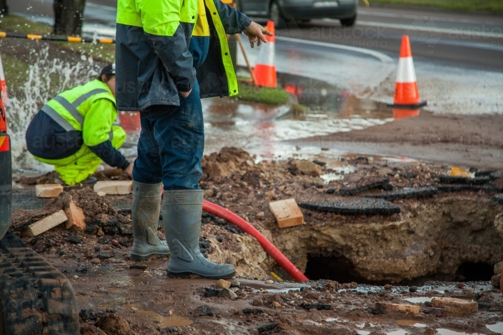 Workers in hi-vis gear standing around a mud hole in the road - Australian Stock Image