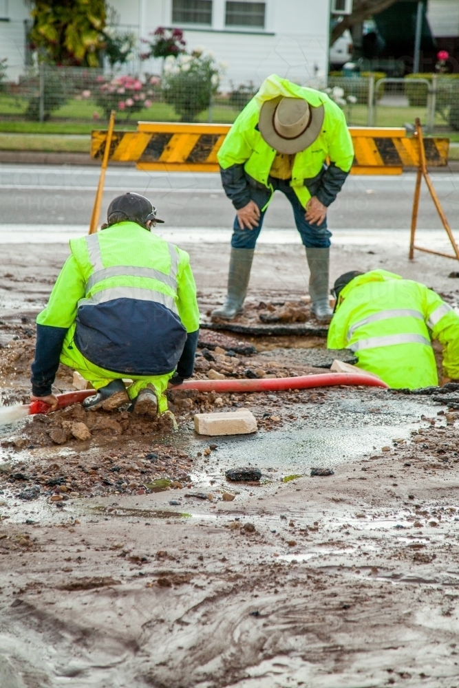 Workers in hi-vis gear standing around a mud hole in the road - Australian Stock Image