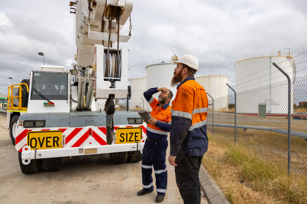 workers looking at the top of pick and carry franna crane truck on industrial site - Australian Stock Image