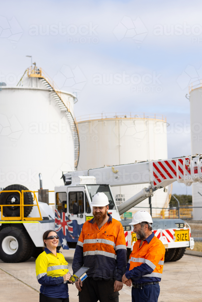 Workers working on digital tablet while standing in front of pick and carry crane machinery - Australian Stock Image