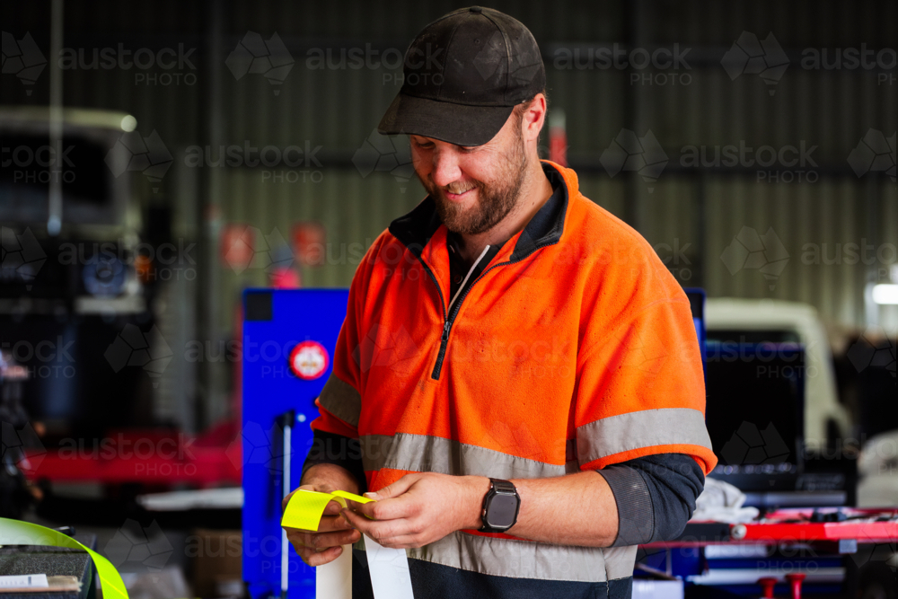 Workman cutting reflective tape for installation on mining fleet vehicle for safety in workshop - Australian Stock Image