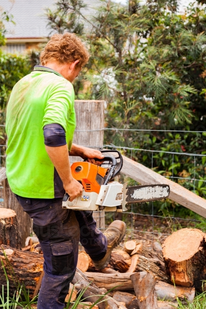 Workman using a chainsaw to cut logs into smaller rounds of wood - Australian Stock Image