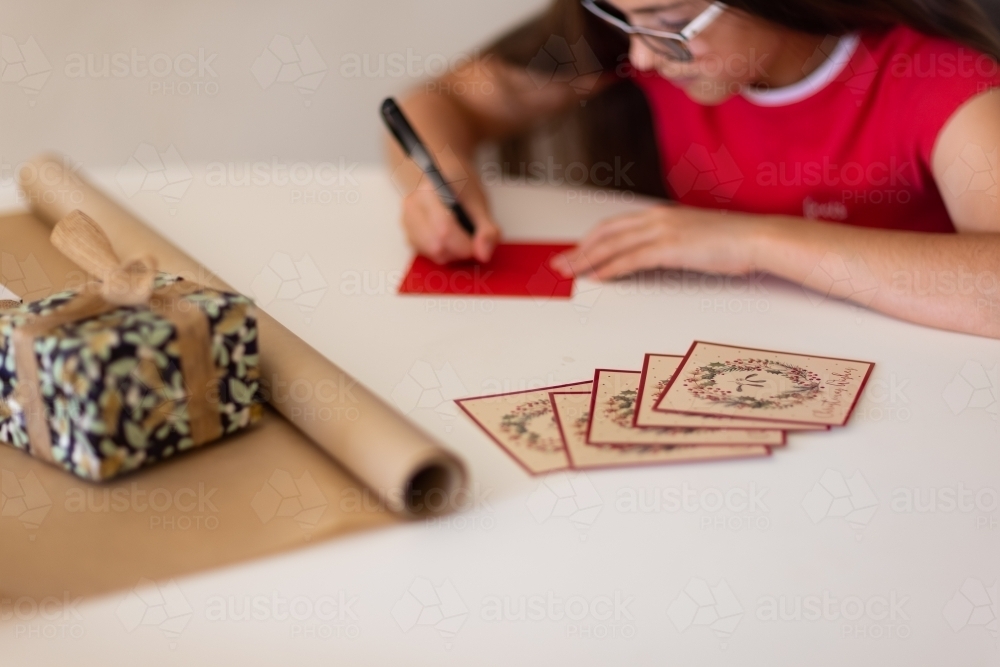 wrapping paper and cards in foreground with girl writing on envelope - Australian Stock Image