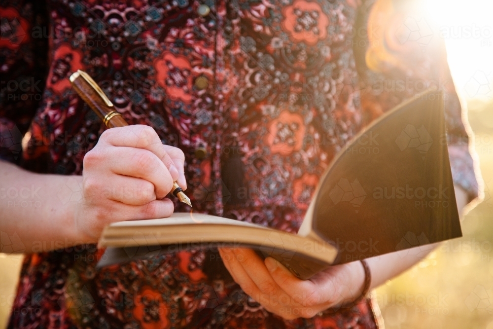 Writer holding journal and fountain pen with sun flare - Australian Stock Image