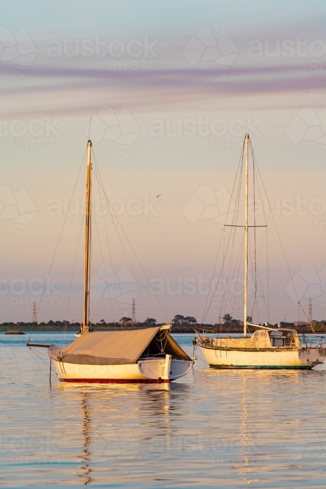 Yachts and their reflections on calm water in late afternoon light. - Australian Stock Image
