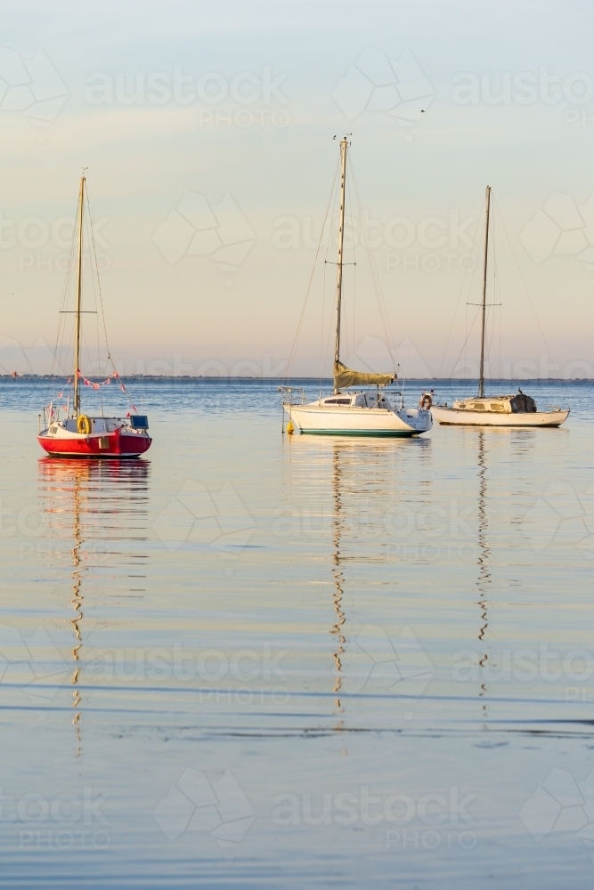 Yachts and their reflections on calm water in late afternoon light. - Australian Stock Image