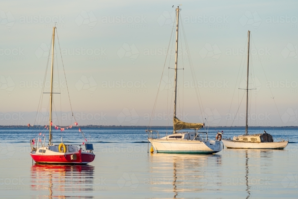 Yachts and their reflections on calm water in late afternoon light. - Australian Stock Image