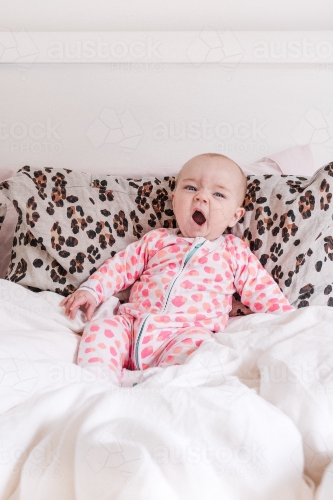 Yawning baby reclining in bed. - Australian Stock Image