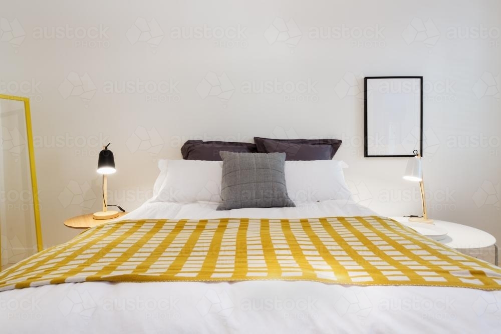 Yellow accent decor throw rug in contemporary styled white bedroom - Australian Stock Image