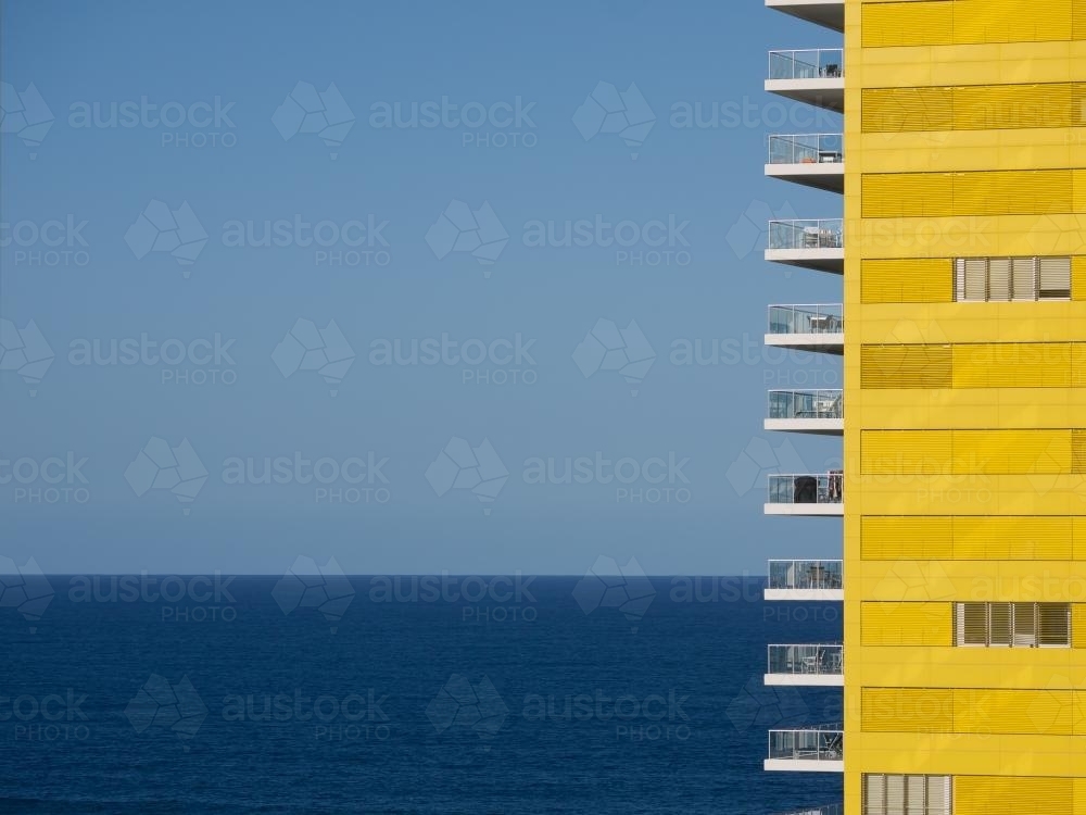 Yellow apartment building with blue sky and sea - Australian Stock Image