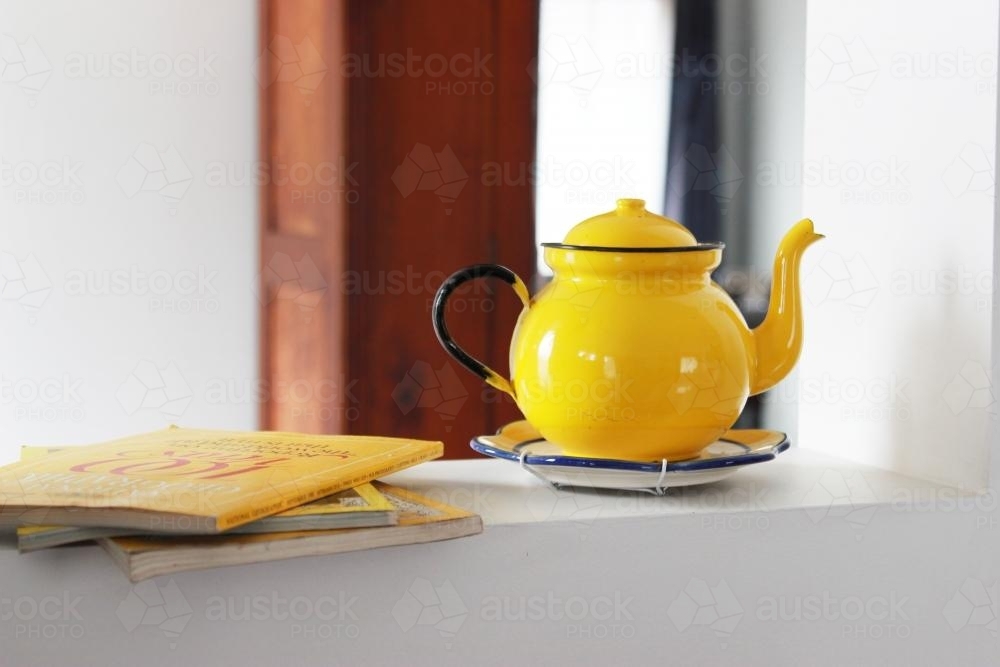 Yellow books and teapot on a shelf inside a house - Australian Stock Image