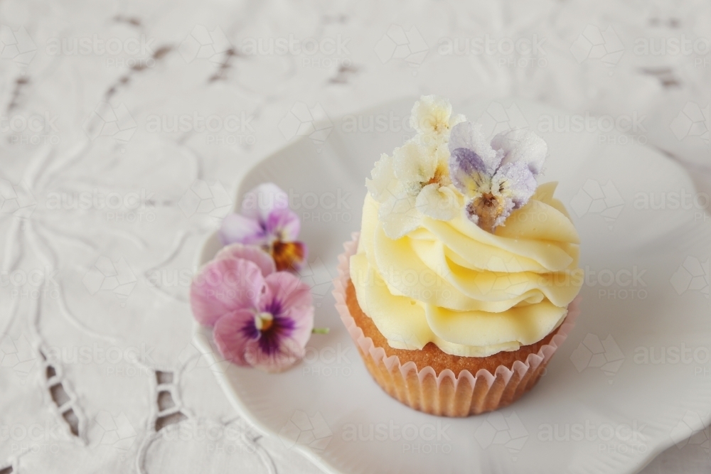 Yellow cupcakes with sugared edible flowers on vintage plate - Australian Stock Image