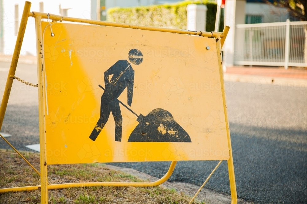 Image of Yellow digging road work sign near construction site on footpath Austockphoto