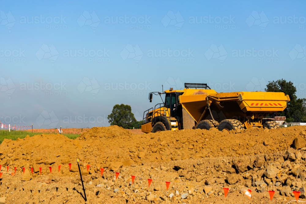 Yellow dump ruck beside dirt pile on roadwork construction site for Singleton Bypass - Australian Stock Image