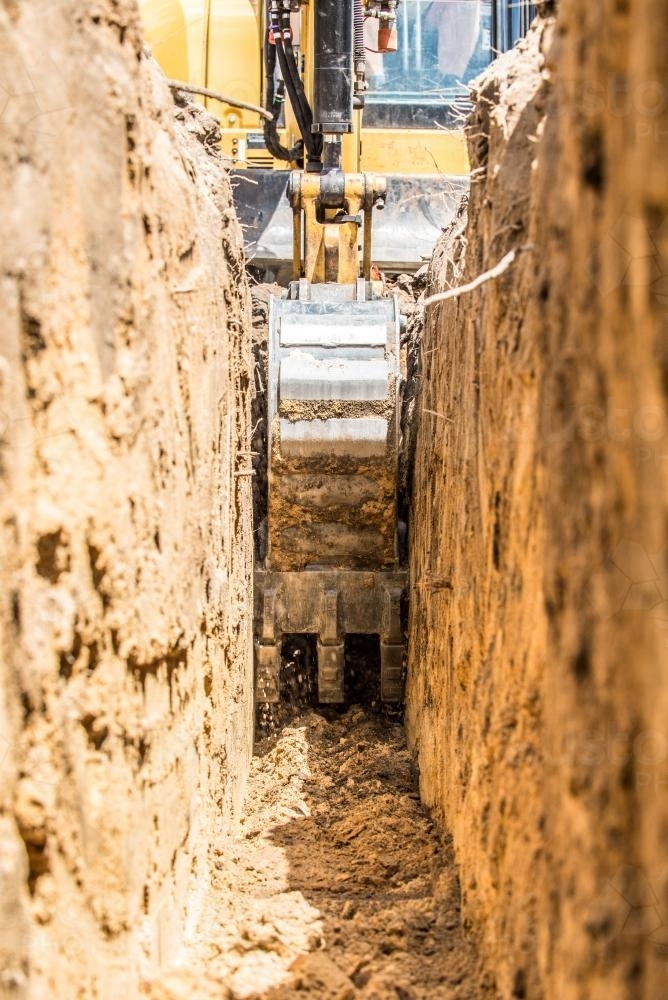 Yellow excavator digging trench with toothed trenching bucket - Australian Stock Image