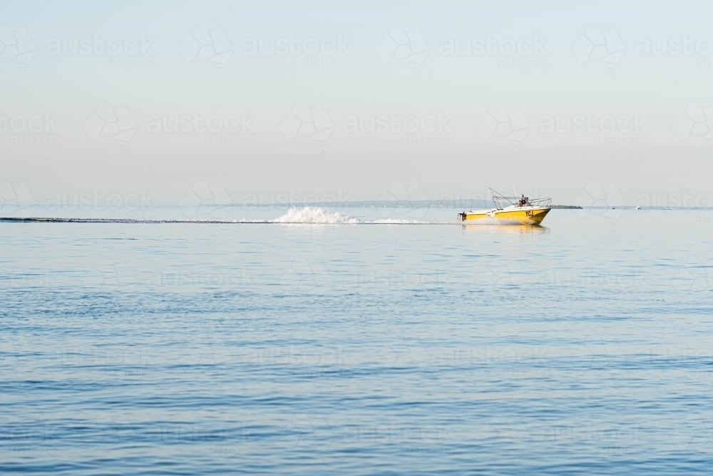 yellow fishing boat cruising along the calm  blue bay - Australian Stock Image