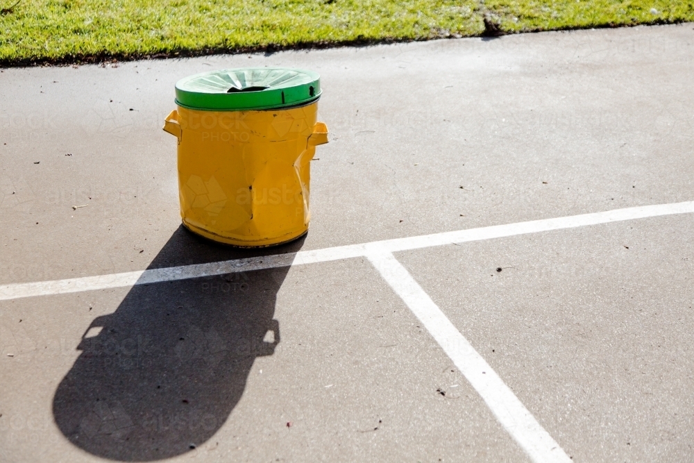 Yellow garbage bin with a green lid outside in a playground - Australian Stock Image
